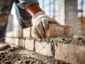 Worker wearing protective gloves carefully laying bricks with mortar to construct a sturdy wall at a construction site in daylight Royalty Free Stock Photo