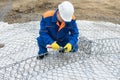 Worker in a white helmet and overalls knits a steel wire structure