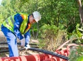 A worker in a white helmet and yellow vest, cuts a plastic pipe with blue scissors