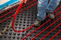 Worker who instal red tubes of radiant underfloor heating installation