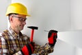 Worker in a yellow helmet and red gloves is holding a hammer