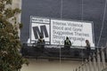 Workers on catwalk paint sign advertising M-rated film in Los Angeles.