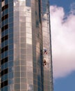 Workers clean windows of tall building under blue sky with clouds in the background Royalty Free Stock Photo