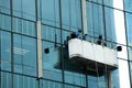 Workers crane cradle clean windows glass of high