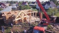 Workers with crane lift wooden structure of house. Clip. Top view of process of installing facade of wooden roof with