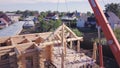 Workers with crane lift wooden structure of house. Clip. Top view of process of installing facade of wooden roof with