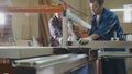 Workers at factory are cutting wooden fragment on electric saw at furniture industry