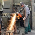 Workers in a foundry grind castings with a grinding machine - He