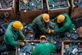 Workers in green uniforms and yellow helmets sort through piles of discarded electronics in a recycling facility Royalty Free Stock Photo