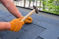 Workers hands installing bitumen roof shingles using hammer in nails