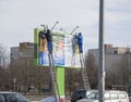 Workers hang an advertising banner at a height from the ladders