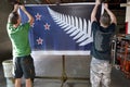 Workers hang aprint of the Silver Fern (Black, White and Blue) f