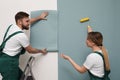 Workers hanging stylish wall paper sheet on light