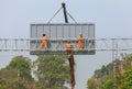 Workers install big steel billboard over highway