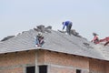Workers installing concrete tiles on the roof while roofing house