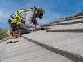Workers are installing gray roof tiles wearing seat belts to ensure safe working at heights