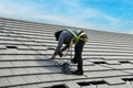 Workers are installing gray roof tiles wearing seat belts to ensure safe working at heights