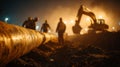 Workers installing underground pipeline at night construction site with heavy machinery and lights Royalty Free Stock Photo