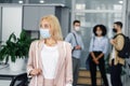 Workers in modern office hallway return to work after quarantine. Focus on beautiful blonde woman in business suit and