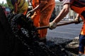 Workers in orange uniform are laying hot asphalt on a city street. Road repair