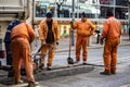 Workers in orange uniforms and protection equipment fixing and patching damaged road