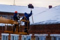 Workers in overalls and orange helmets on the crane basket remove icicles from roof of the house on a winter day - cleaning the