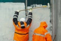 Workers paint wall. Wall flogging. Orange clothing of workers. Smearing graffiti