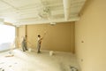 Workers painting a beige wall in a modern office space during daylight hours Royalty Free Stock Photo