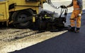 Workers regulate tracked paver laying asphalt