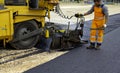 Workers regulate tracked paver laying asphalt