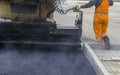 Workers regulate tracked paver laying asphalt heated