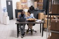 Workers sitting at table in storehouse checking transportation logistics on laptop computer Royalty Free Stock Photo