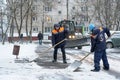 Workers in uniform with big shovels, a tractor removes snow from the road. Snow removal on the city streets Royalty Free Stock Photo