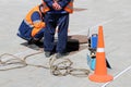 Workers in uniform stand over the open sewer hatch on a street