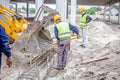 Workers are unloading concrete with shovel from excavator`s fron