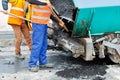 Workers use shovels to clean an asphalt paver bucket for the subsequent asphalt paving of a new section of the road