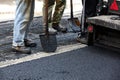 Workers using asphalt paver tools during road construction.