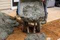 Workers are using a wheelbarrow to shovel wet cement onto the sidewalk path near house by pouring wet cement concrete Royalty Free Stock Photo