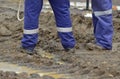 Workers wearing overalls and workboots stand in a muddy environment