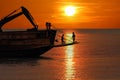 The workers are working to adjust mooring buoy on the vessel and truck excavator in the ocean at sunset Royalty Free Stock Photo