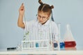 Workes with liquid that is in test tubes. Little girl in coat playing a scientist in lab by using equipment Royalty Free Stock Photo