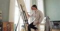 Woman paintress is painting picture using brush on canvas sitting near easel.