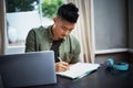 Working according to the design brief. a handsome young man taking notes while working on his laptop at home.