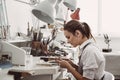 Working all day. Side view of young female jeweler sitting at her jewelry workshop and holding in hands jewelry tools Royalty Free Stock Photo