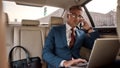 Working Anywhere. Confident and stylish mature businessman in full suit working on his laptop and talking on the phone Royalty Free Stock Photo