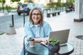 Working from anywhere, smiling and happy mature woman working on laptop from cafe on street. Freedom and flexibility Royalty Free Stock Photo