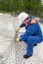 Working in a blue uniform and a white helmet, knit mesh for cells under the stones to improve the shore