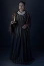 A working class Victorian woman holding a candle in the dark against a grey studio backdrop