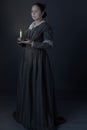 A working class Victorian woman holding a candle in the dark against a grey studio backdrop Royalty Free Stock Photo