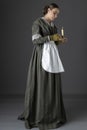 A working class Victorian woman wearing a dark green check bodice and skirt with an apron and holding a candle. Royalty Free Stock Photo